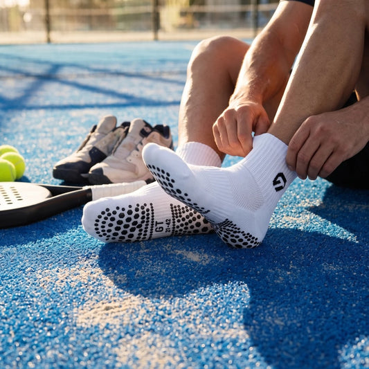 Padelspeler trekt witte GT Ankle Grip Socks aan op de padelbaan, antislip padelsokken met grip onder de zool | GT Sport Selection